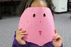 Child holding a face mask at Family Arts Saturday