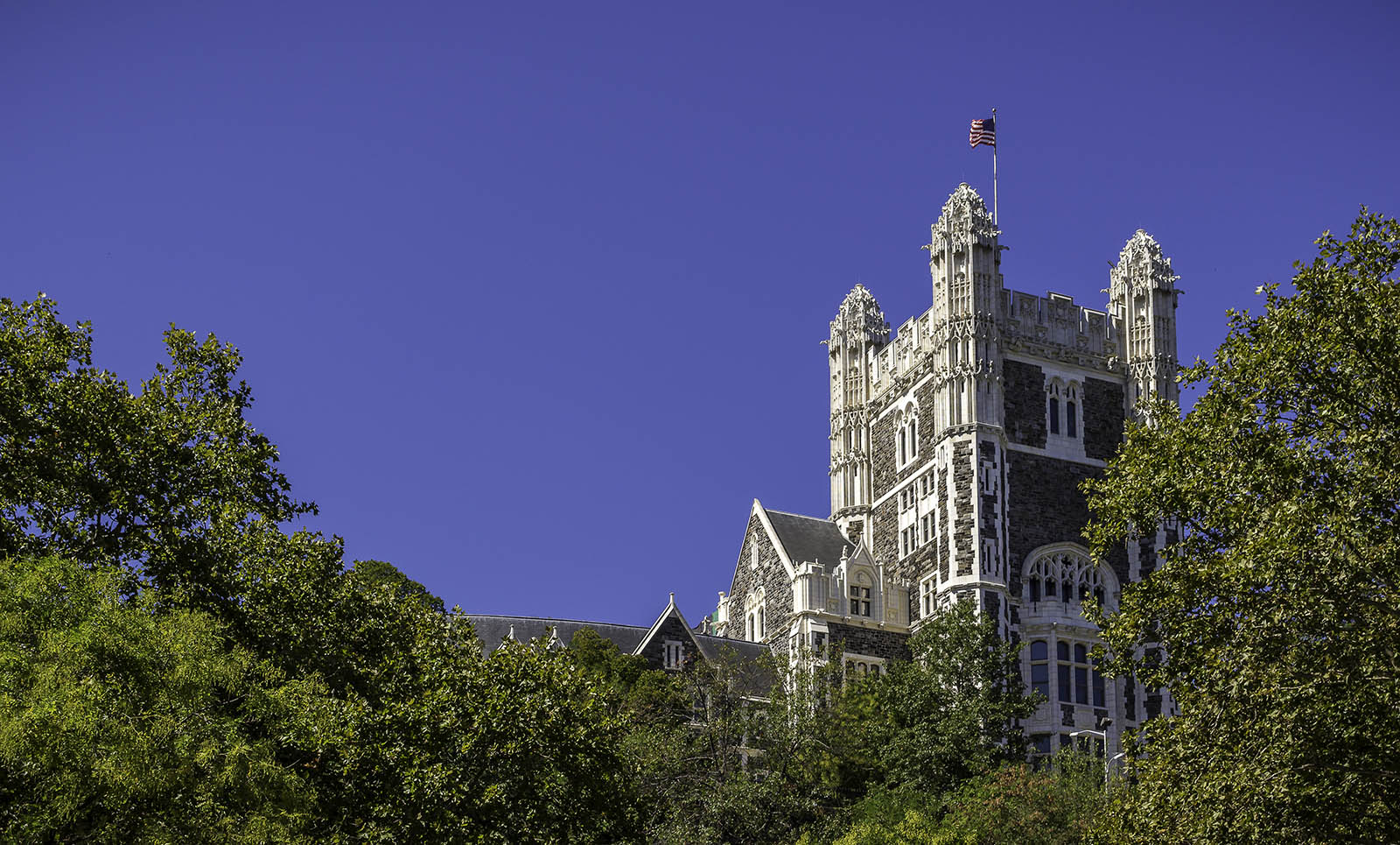 Shepard Hall tower with American flag flying and leafy trees below