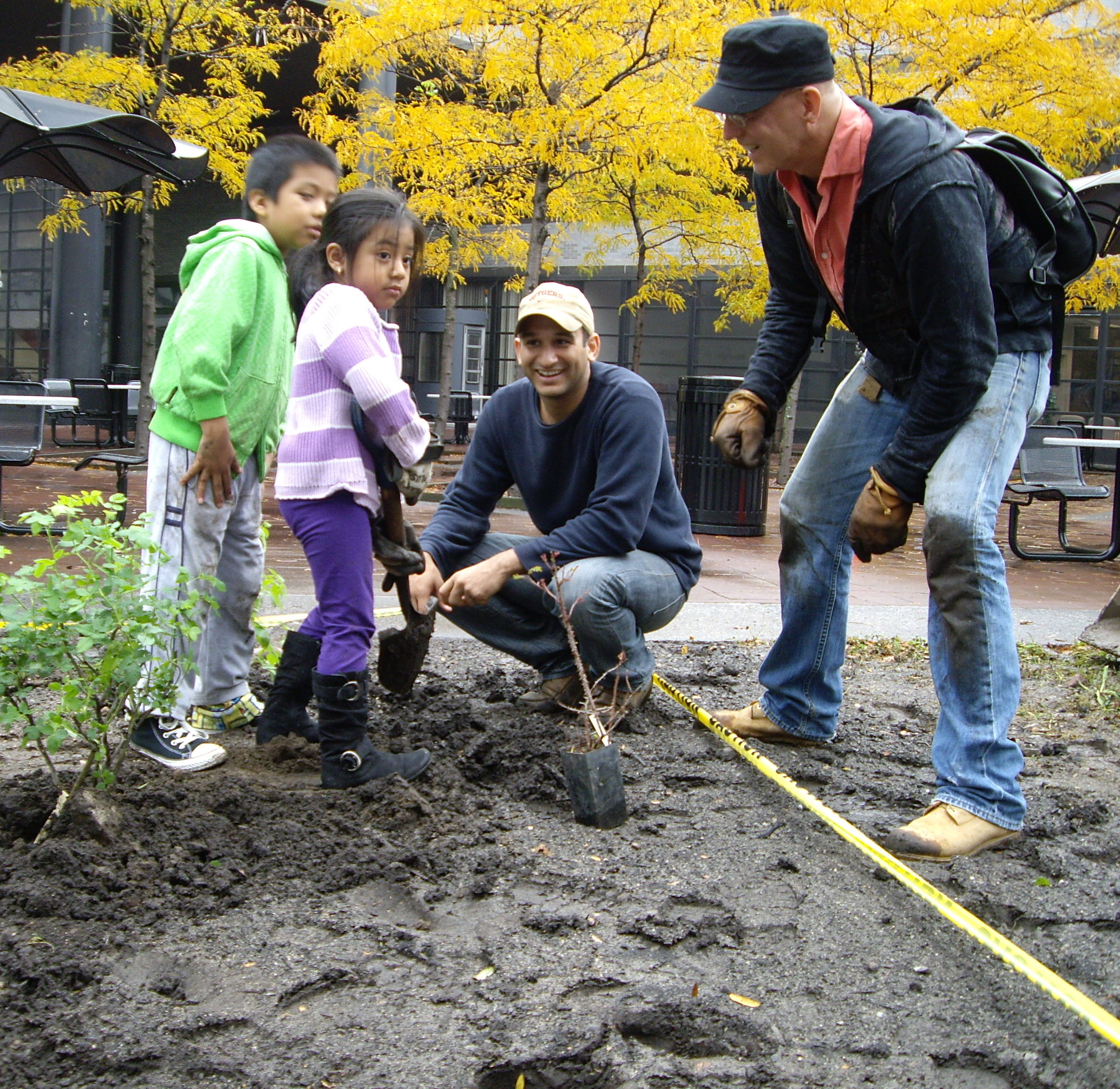 Two young residents help Paimaan Lodhi [middle], Urban Planner in the Office of the Manhattan Borough President, and Dane Twining of the Heritage Rose Foundation at the heritage rose planting at CCNY. 