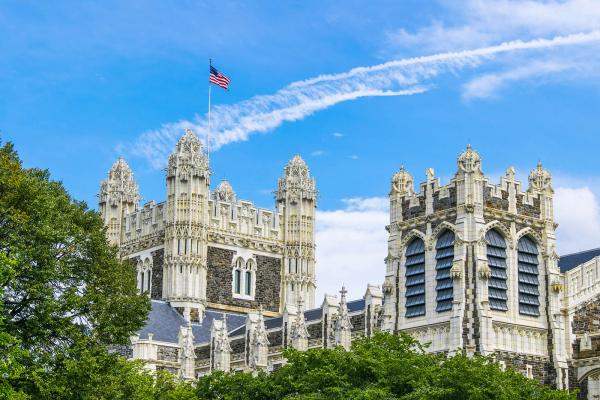 Shepard Hall towers and roofline with American flag and trees