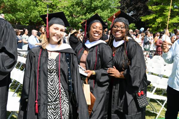 3 Students in Full Regalia Smiling as they wait to be seated for Commencement Ceremony