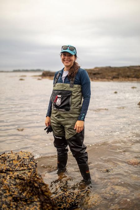 Photo of Melina Giakoumis standing in water with a cap and sun glasses on head.