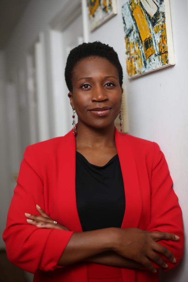 Dr. Onyinye Balogun in a red blazer, smiling and looking straight at the camera with arms crossed.