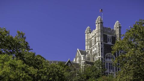 Shepard Hall tower with American flag flying and leafy trees below