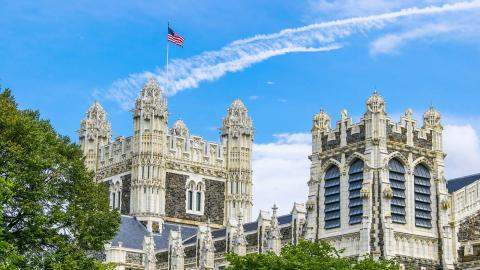 Shepard Hall towers and roofline with American flag and trees