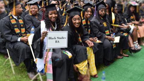 Students at the 2018 Graduation- they are all in cap and gown- about 30 people are int he photo but 5 are looking into the camera- they are holding a sign that reads " Black Studies BA" 