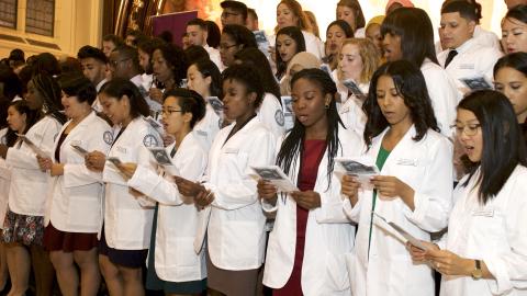 students wearing white coats at a ceremony in the great hall of shepard hall