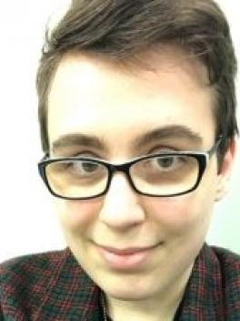 A profile photo of a young white woman with brown hair and glasses. She is smiling and wearing a red and green blazer over a black T-shirt.